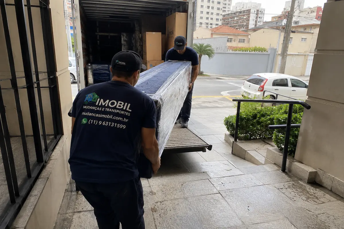 Equipe da Imobil Mudanças transportando móvel embalado entre a residência e o caminhão em São Paulo